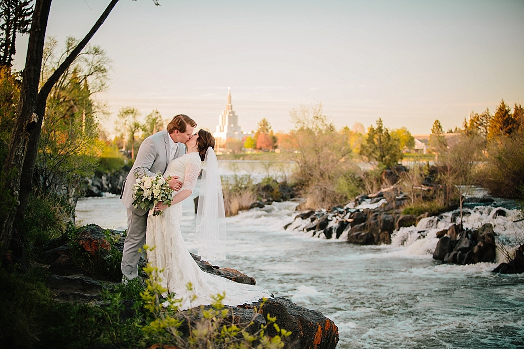 bride and groom kissing by water with a view of Idaho Falls temple