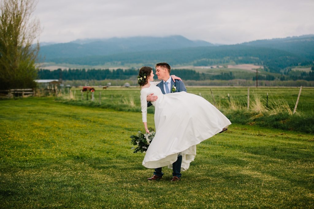groom lifting bride up in grassy field during Minimalistic and Earthy Idaho Falls Wedding portraits