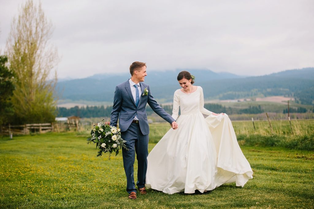 couple walking hand in hand through beautiful grassy field wearing wedding attire