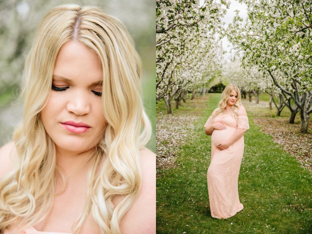 woman standing in apple blossoms with hands holding pregnant belly