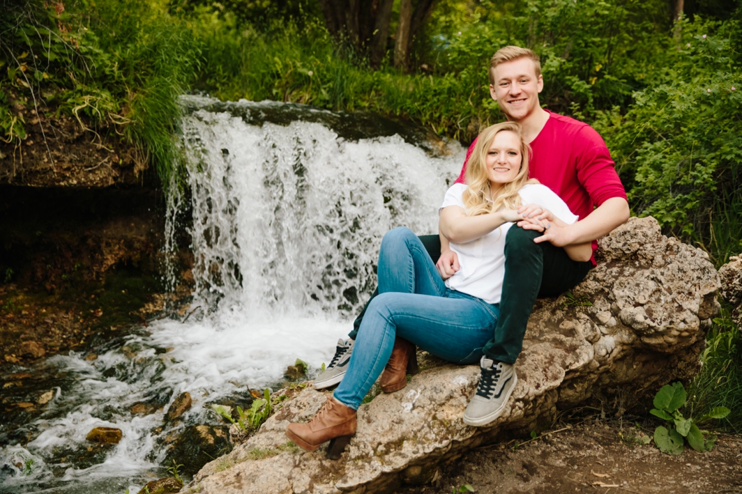 Jackson Hole photographer captures man and woman sitting together by waterfall during downtown Logan Utah engagements