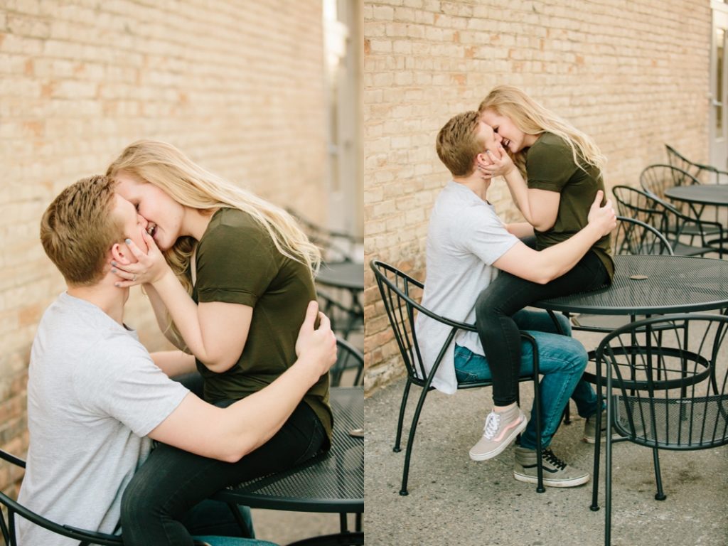 woman sitting on table leaning down to kiss fiancé e 