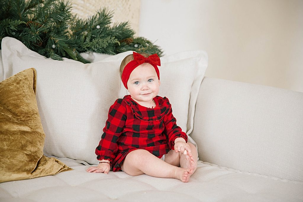 little girl sitting on couch looking at camera wearing red plaid pajamas
