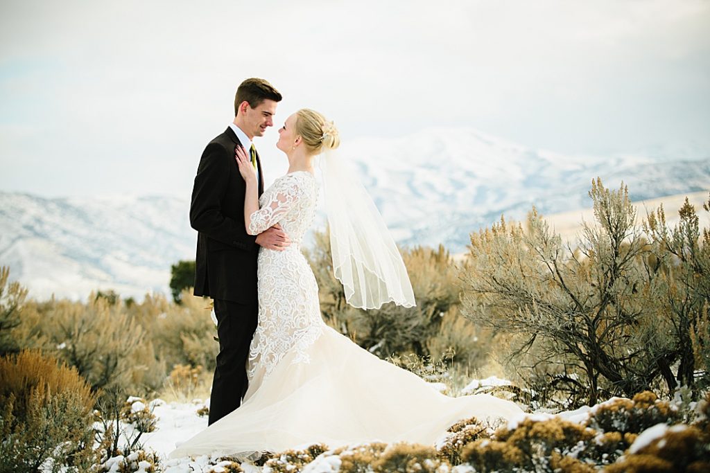 Snowy Pocatello wedding bride and groom standing on lava rock with mountains behind them