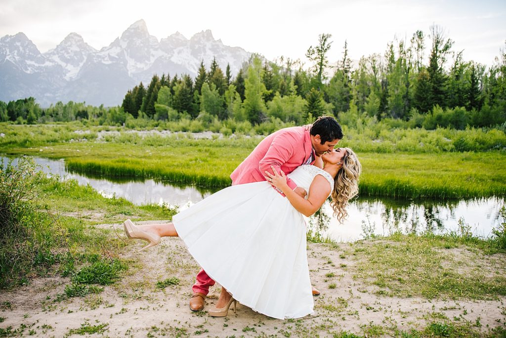 groom in a pink suit dipping his bride in front of the Tetons in Jackson Hole for their summer wedding