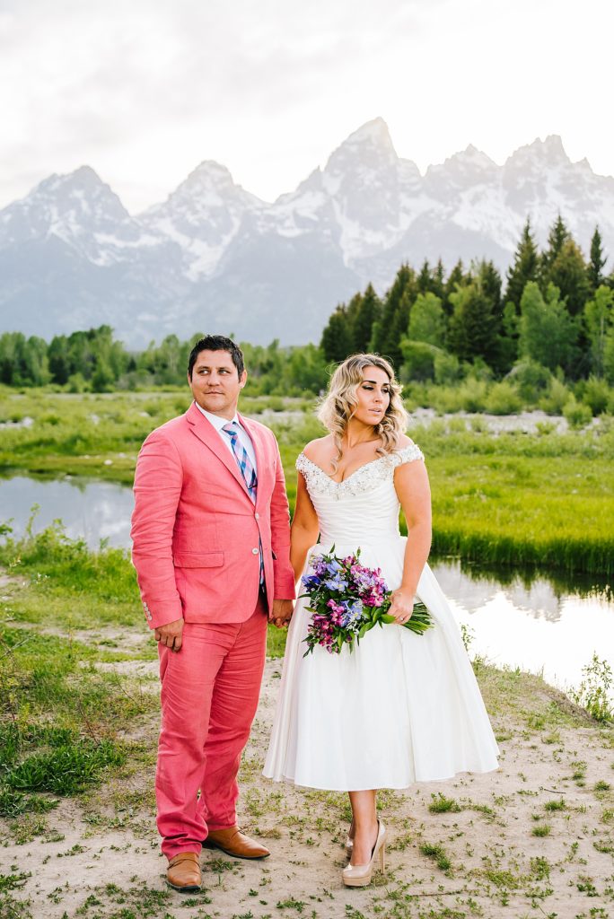 bride and groom holding hands and looking opposite ways with the Tetons behind them