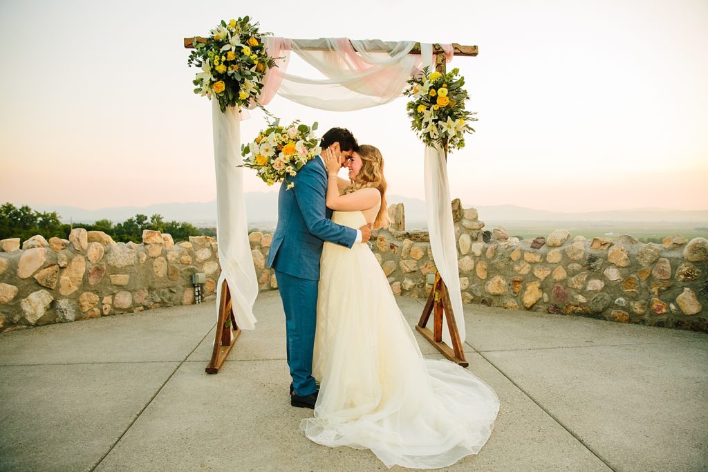 bride and groom embracing at their outdoor wedding ceremony arch 