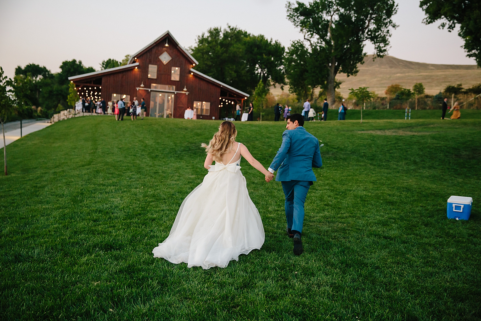 bride and groom holding hands while running up a hill together for their outdoor Idaho wedding 