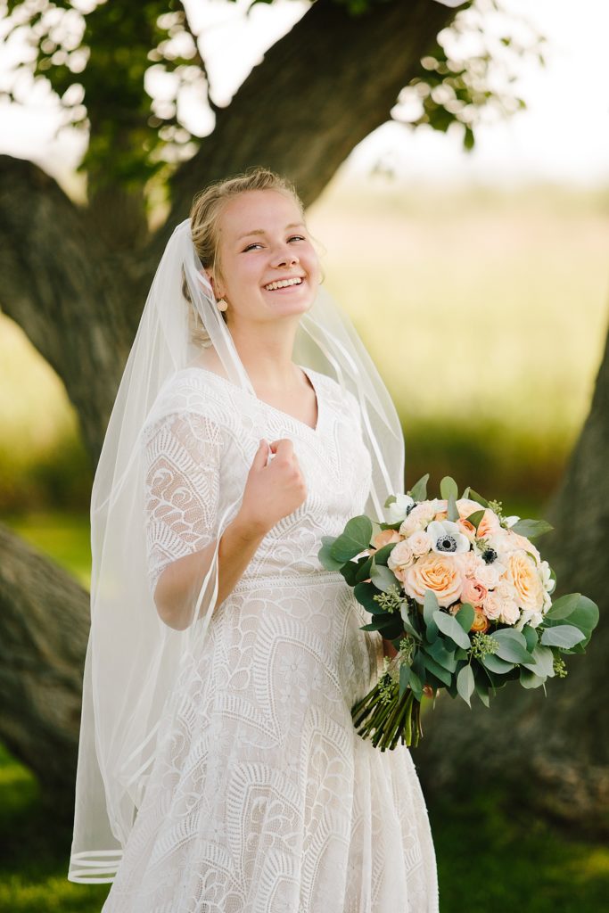 blonde Idaho bride smiling and touching her veil as she holds her bridal bouquet 