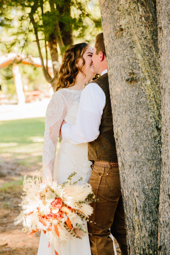 bride and groom kissing behind tree on eagle ridge ranch wedding day