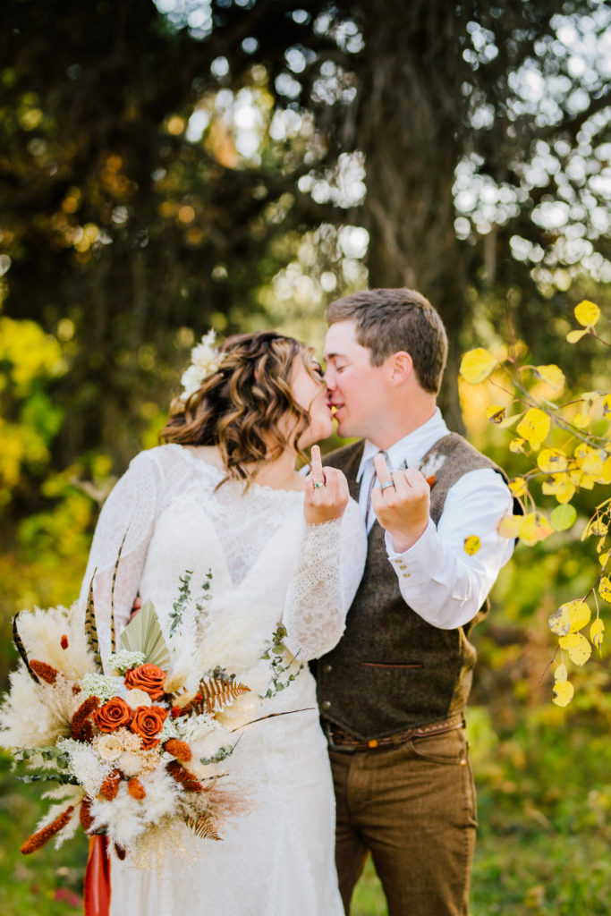 bride and groom holding up ring fingers and kissing during bridal portraits