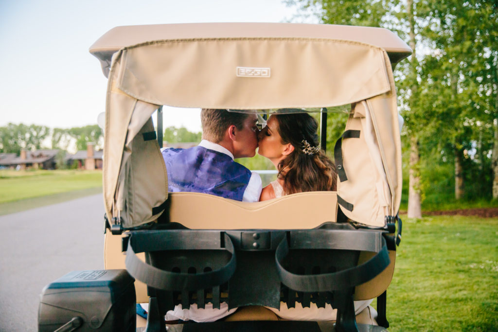 bride and groom kissing in the back of golf cart on wedding day at top Jackson Hole wedding venue
