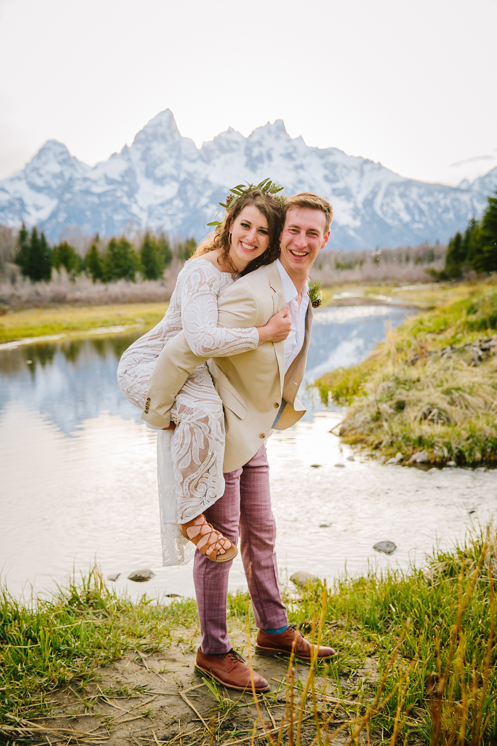 groom giving bride a piggy back ride in the moutnains as the bride wears her lace wedding dress