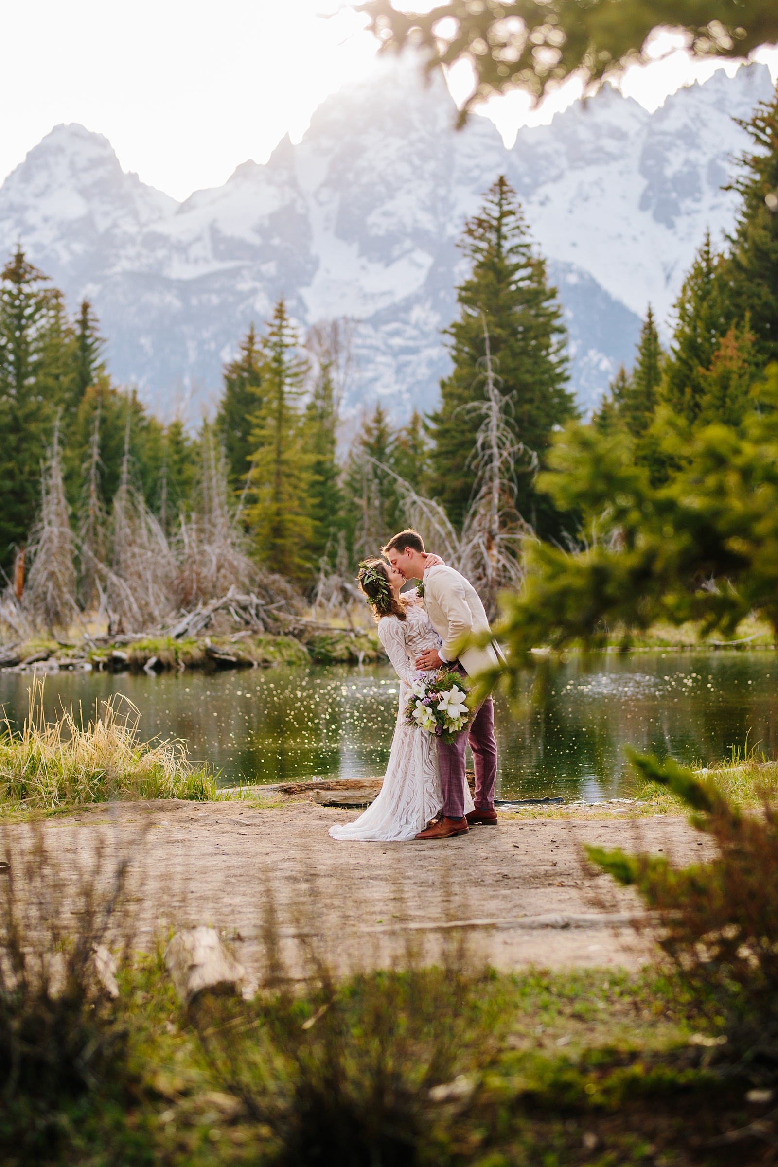 Grand Teton wedding photographers captures bride and groom kissing next to the lake in the woods