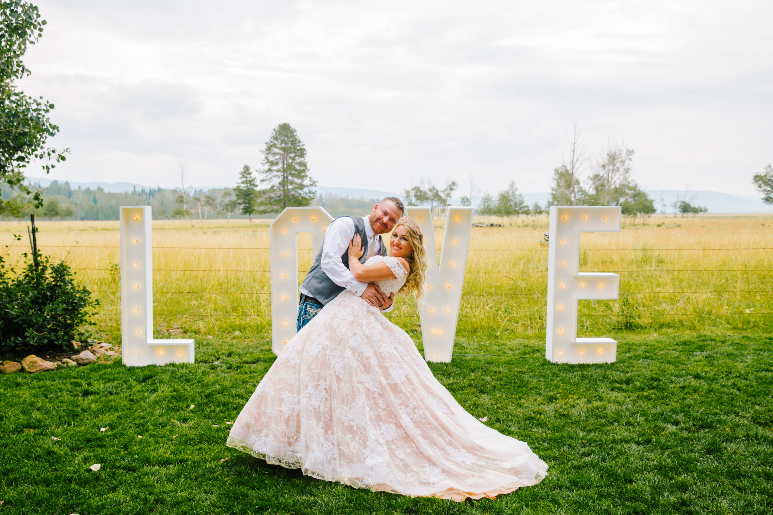 bride and groom kissing as the bride dips back in front of a "LOVE" sign that lights up at their outdoor wedding venue