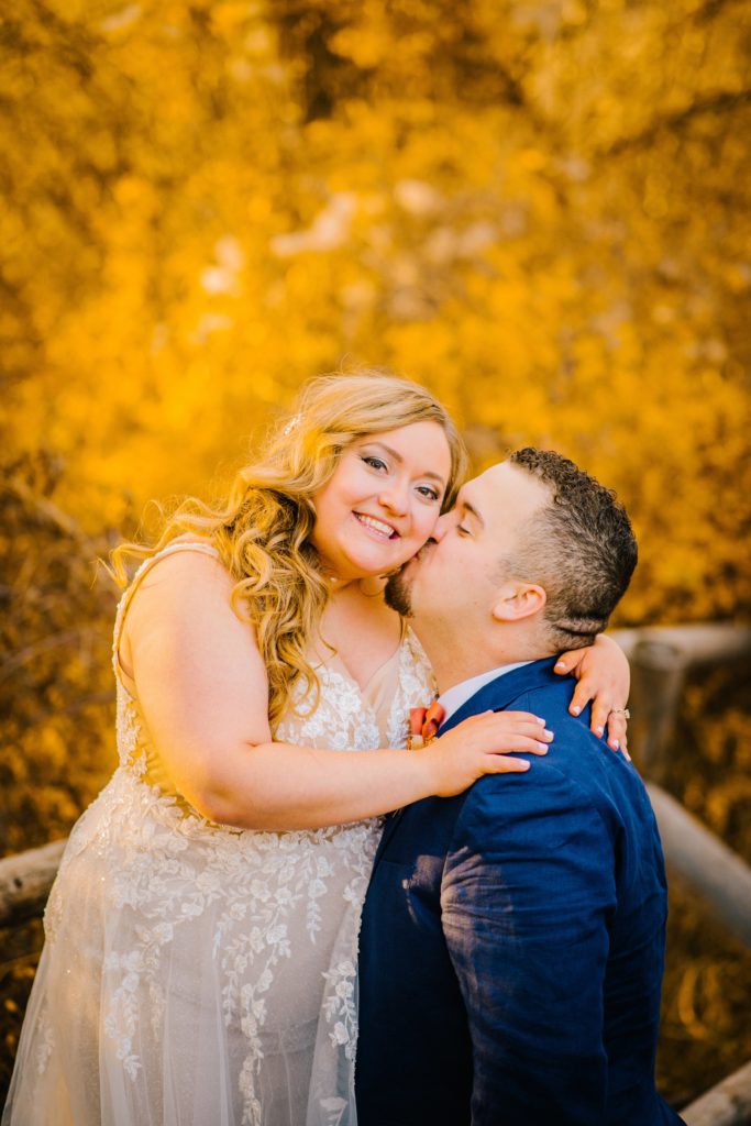 Jackson Hole wedding photographer captures groom kissing bride's cheek during fall portraits