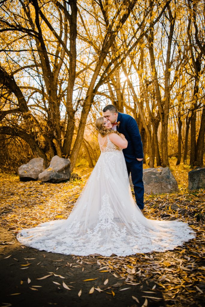 Jackson Hole wedding photographer captures bride and groom dancing in the woods during the fall while kissing as the sun sets through the tree line