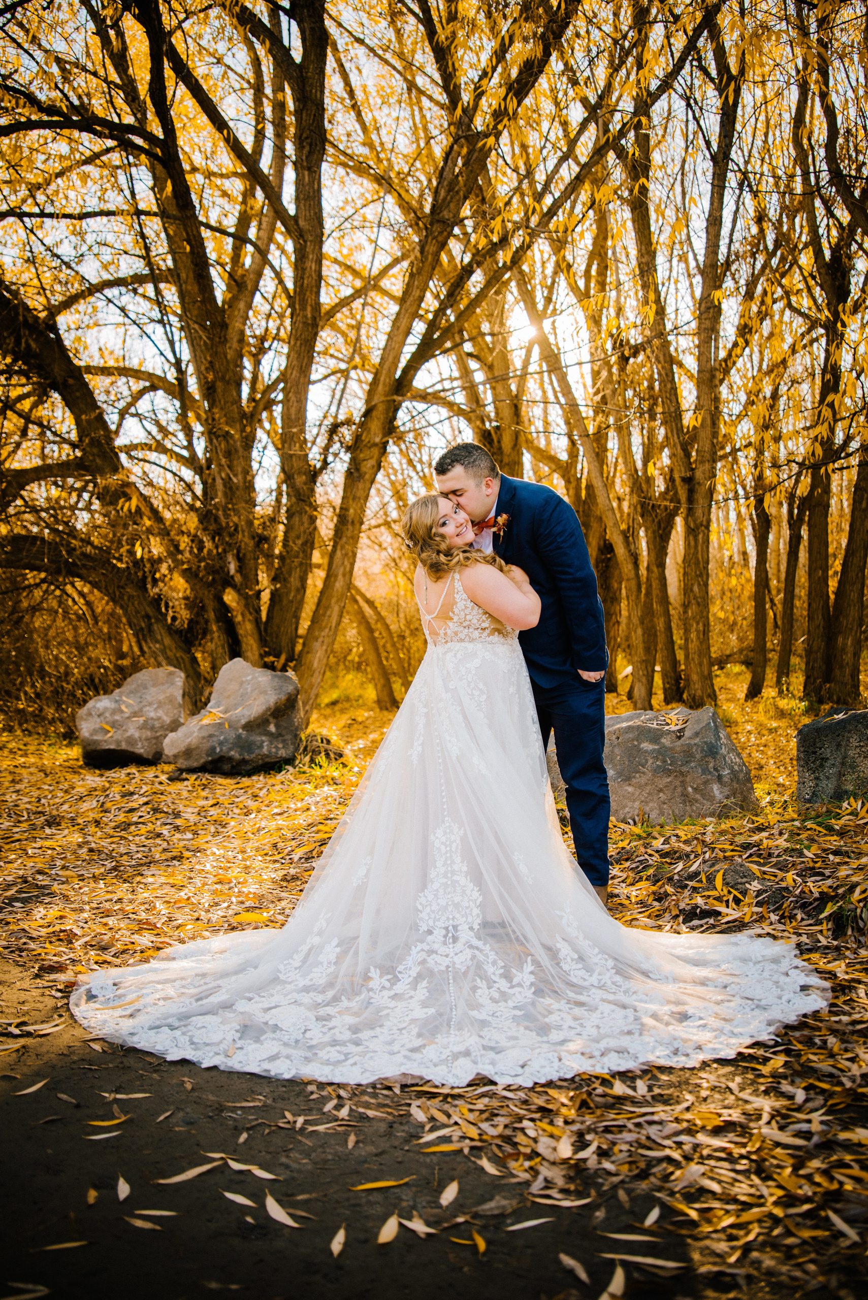 bride and groom dancing in the woods during the fall while kissing as the sun sets through the tree line 