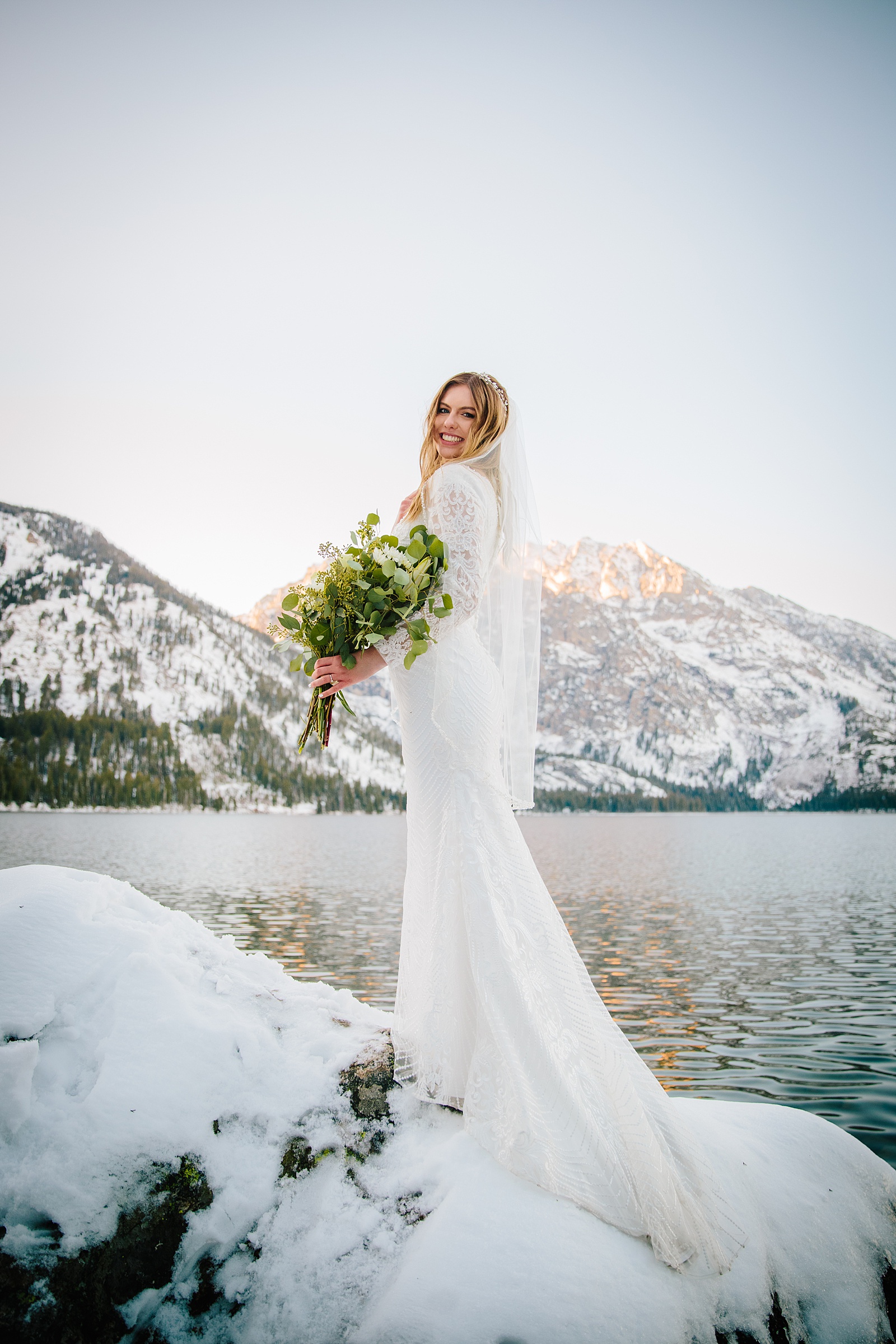 bride on a rock on a lake wearing a long sleeve wedding dress with lace captured by best Pocatello wedding photographer