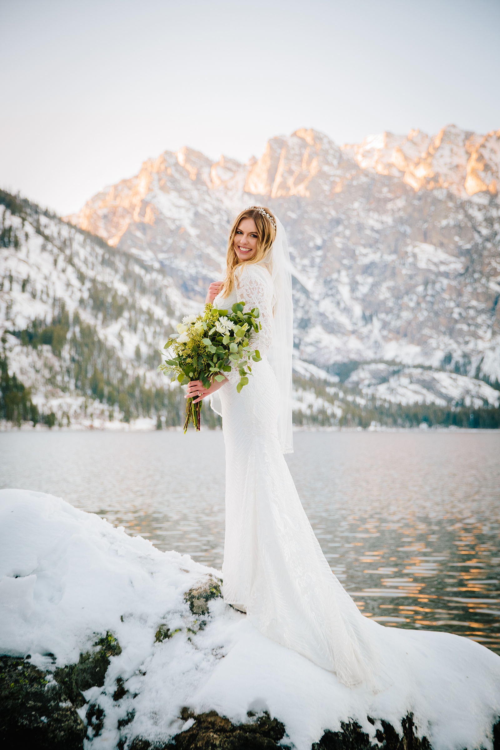 winter bride standing ona rock next to a lake for her Pocatello bridal photos holding her bridal florals as she looks over her shoulder