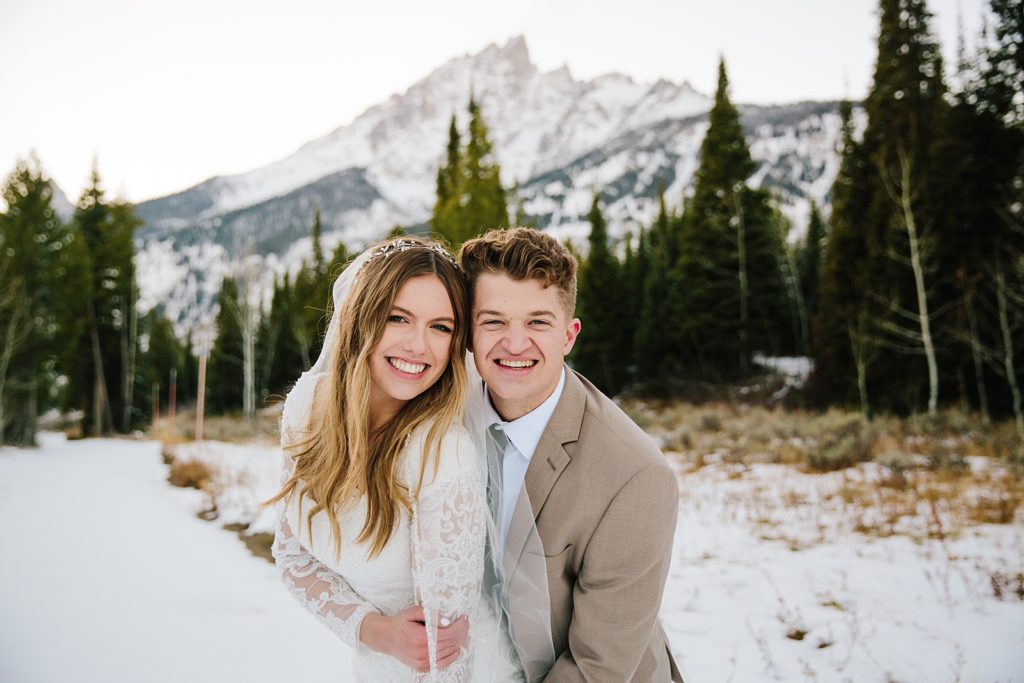 Pocatello wedding photographer captures bride and groom hugging each other during their winter wedding photos and smiling at the camera 