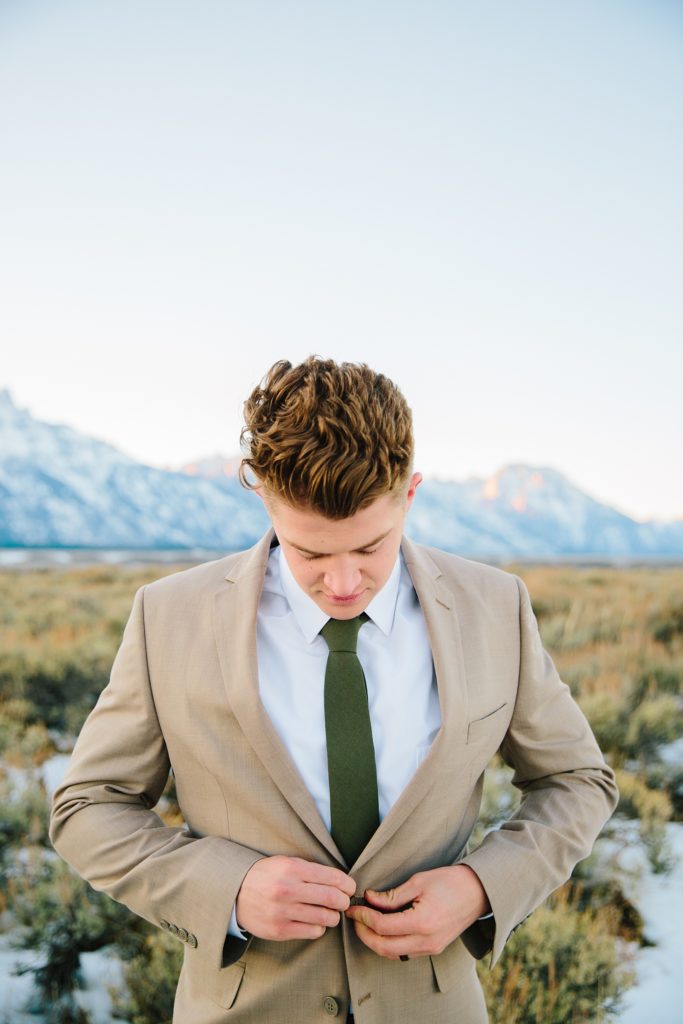 Jackson Hole wedding photographer captures groom buttoning up his tan suit during outdoor bridals