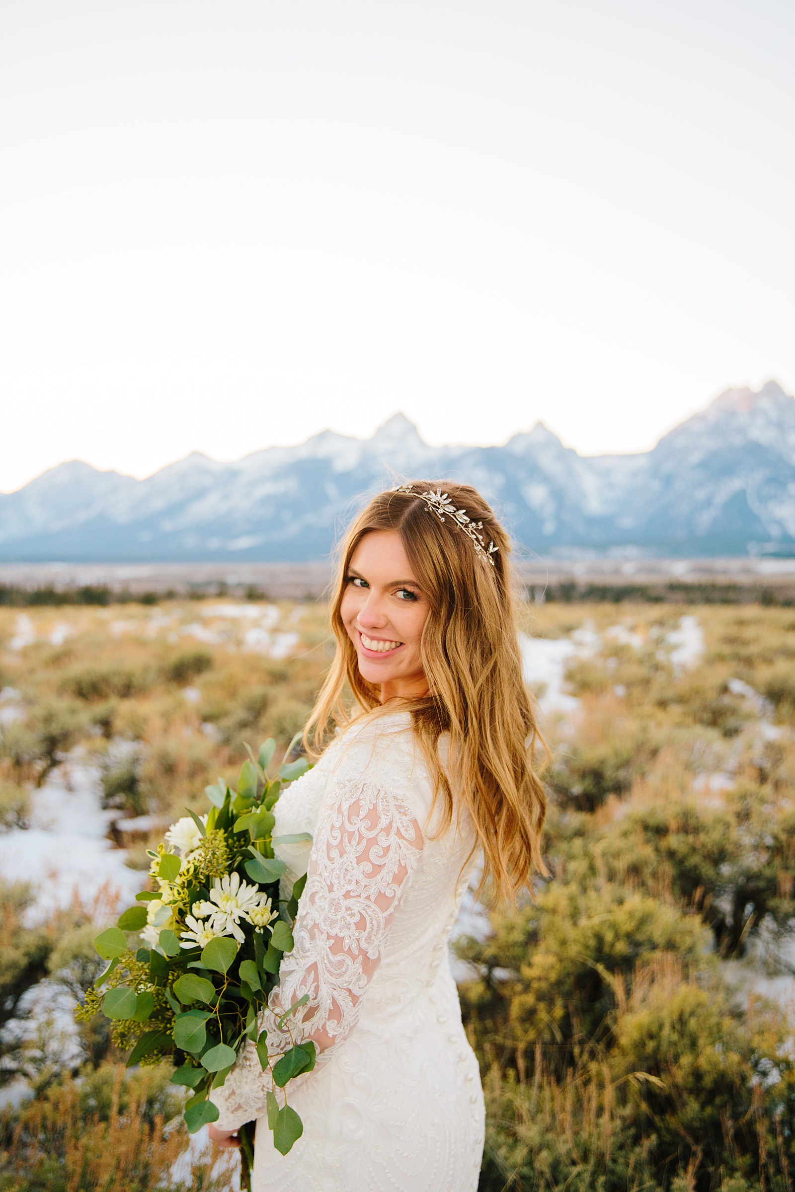 Pocatello Idaho wedding photos with bride in a lace wedding dress holding a white floral and greenery bouquet while smiling over her shoulder
