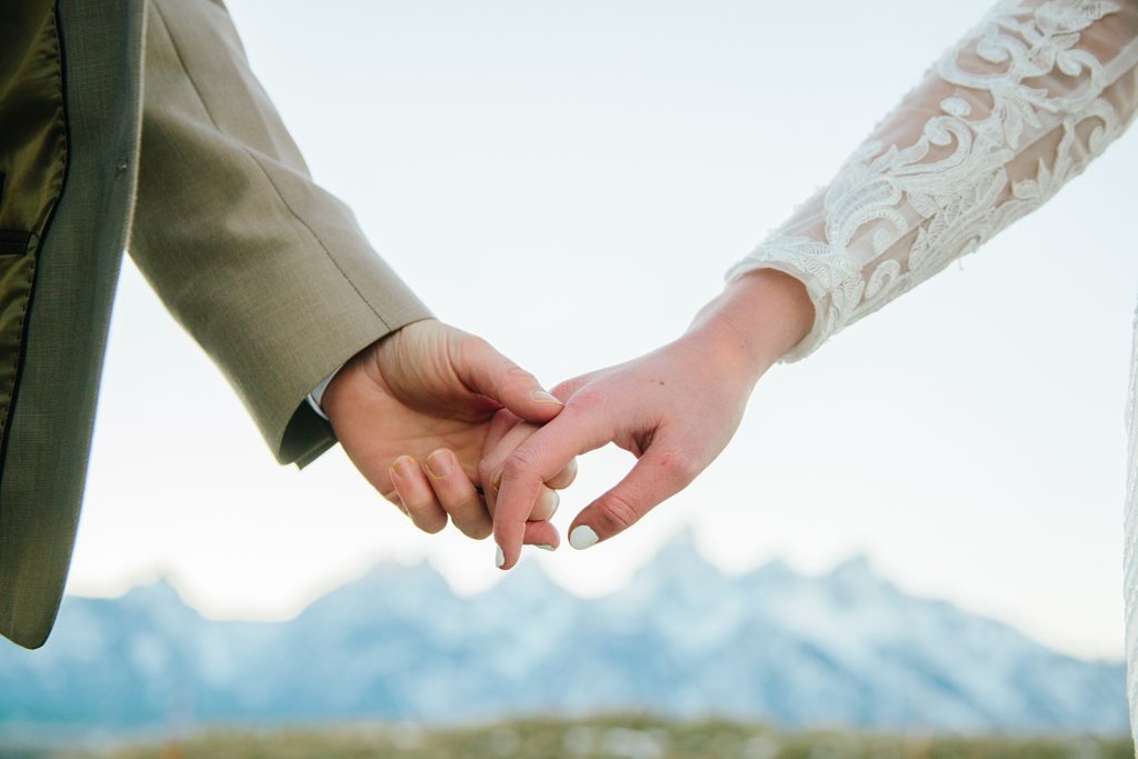 Jackson Hole wedding photographer captures detail shot of bride and groom holding hands together with the mountains in the background for a Pocatello bridal photo