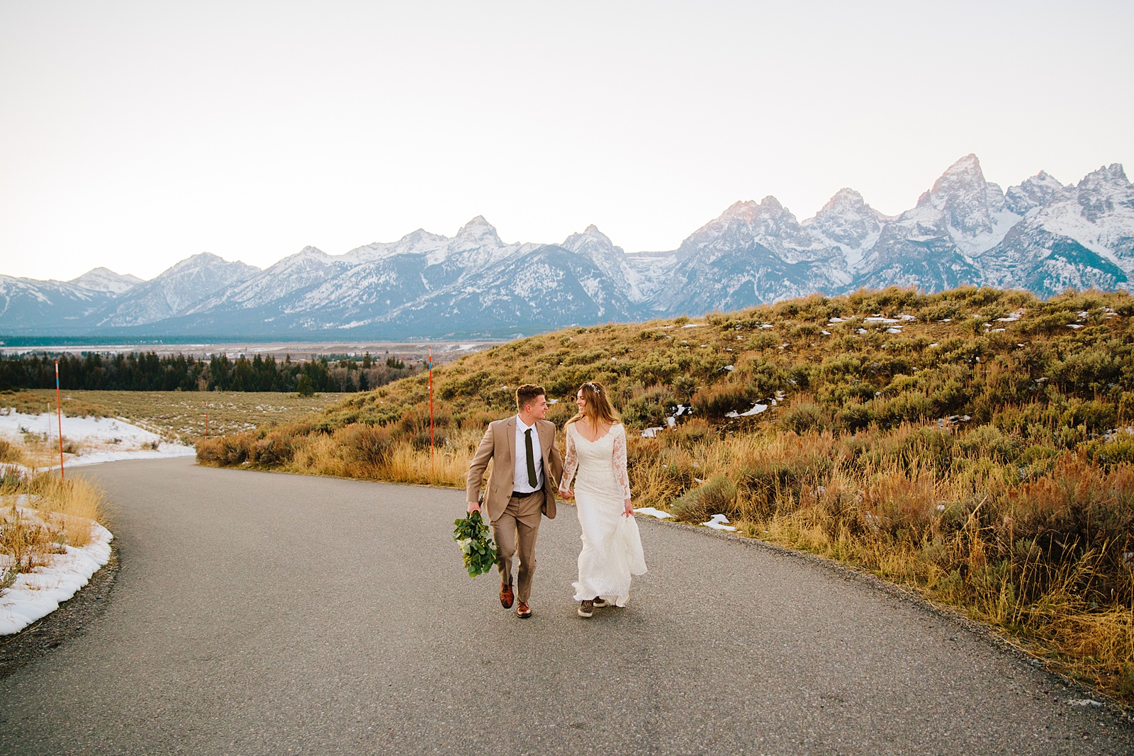 bride and groom holding hands and running down a road together in Pocatello for their bridals portraits