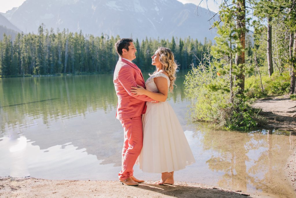 Jackson Hole wedding photographer captures Groom wearing pink suit hugging bride at Jackson hole elopement