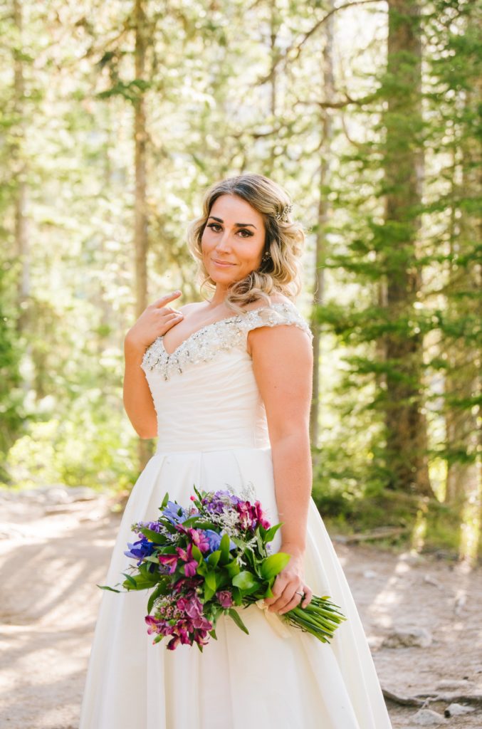 Jackson Hole wedding photographer captures bride standing in forest holding bouquet