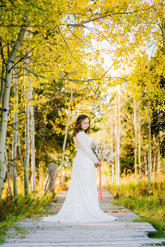 bride in a lace wedding dress walking on a dirt path holding a fall wedding bouquet 
