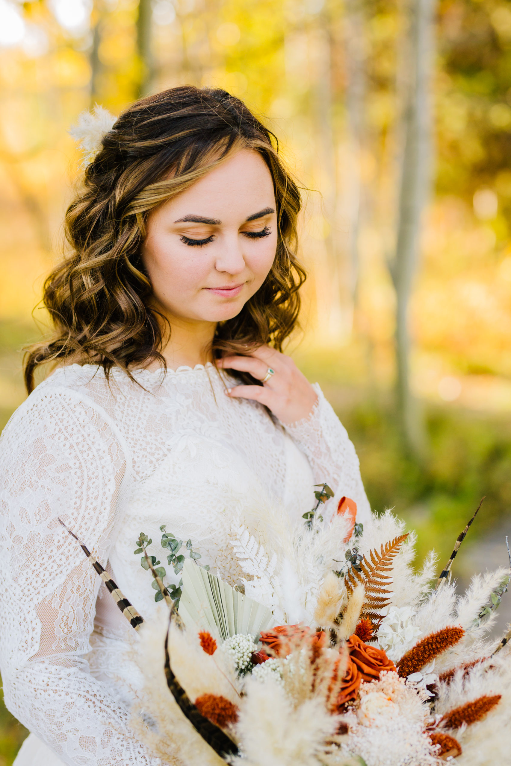 bride in a lace wedding dress and curled hair holding her wedding bouquet and looking down