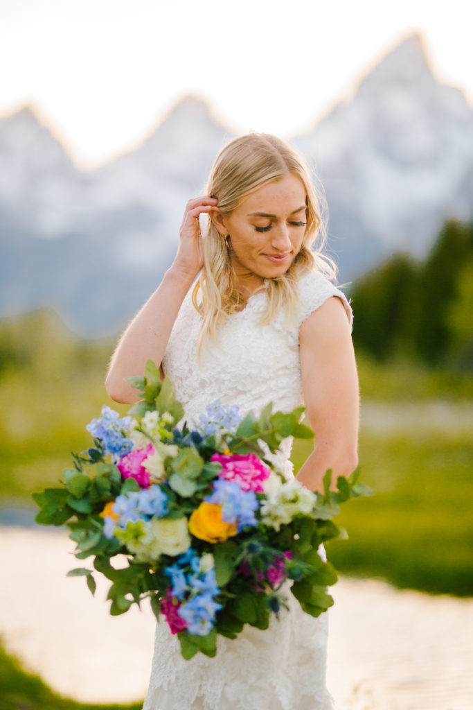 bride in the Tetons posing with her colorful wedding bouquet with the Tetons behind her