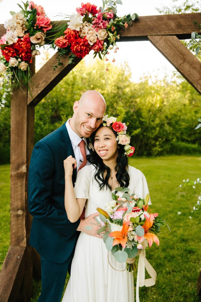 Jackson Hole wedding photographer captures Bride and groom post for photo at alter with orange and red flowers