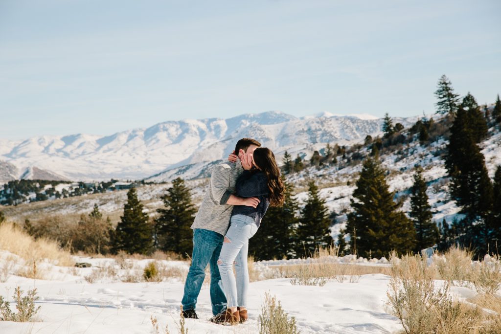 Jackson Hole wedding photographers capture engaged couple kissing in front of snowy mountains