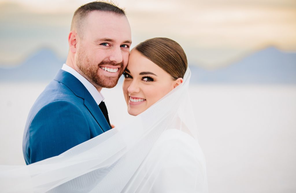 Jackson Hole wedding photographer captures Bride and groom look at camera and smile Dreamy Bonneville Salt Flats Sunset Bridal Wedding Photography