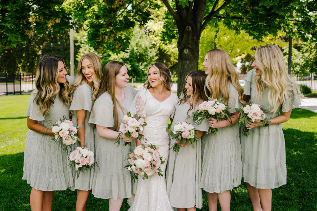 bride with bridesmaids wearing sage green dresses holding bouquets with white and pink florals for summer weddings
