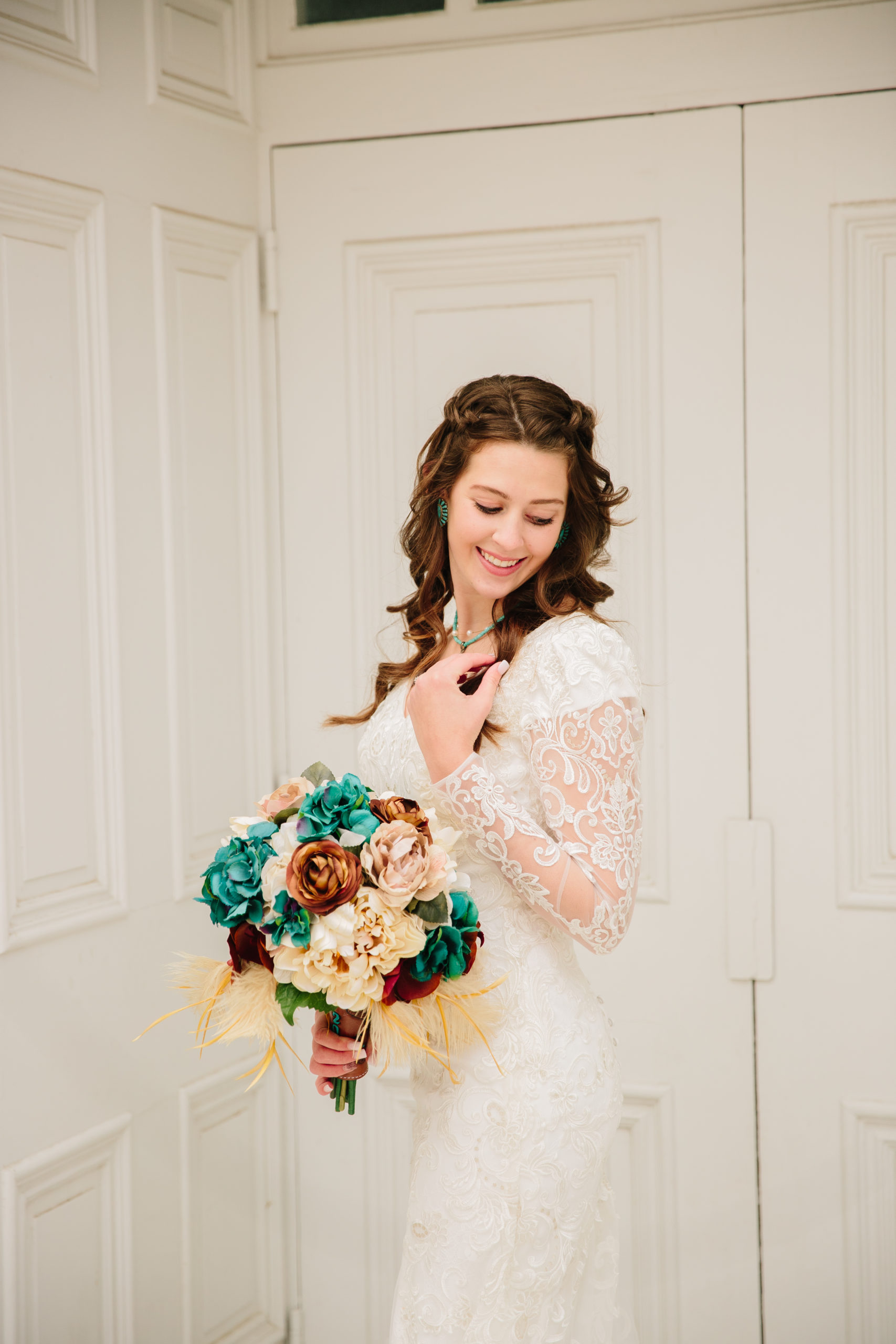 bride standing against a white door as she looks down her shoulder at her florals