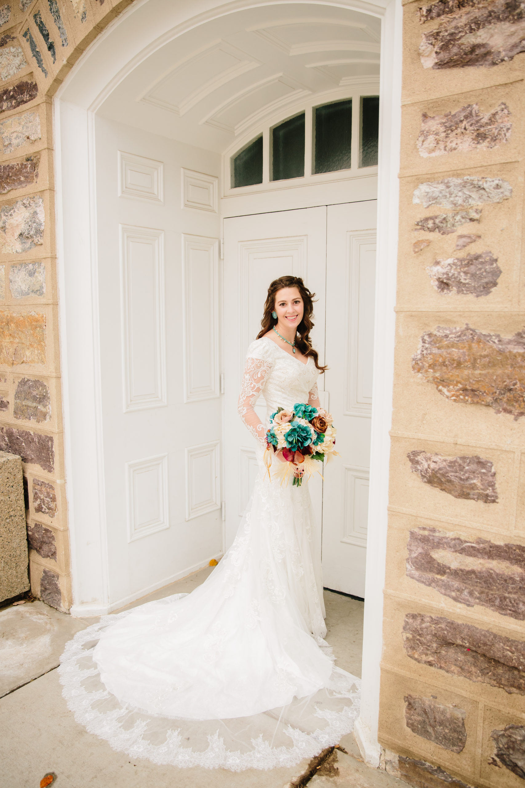 bride standing in an outside doorway while holding her red and blue wedding bouquet