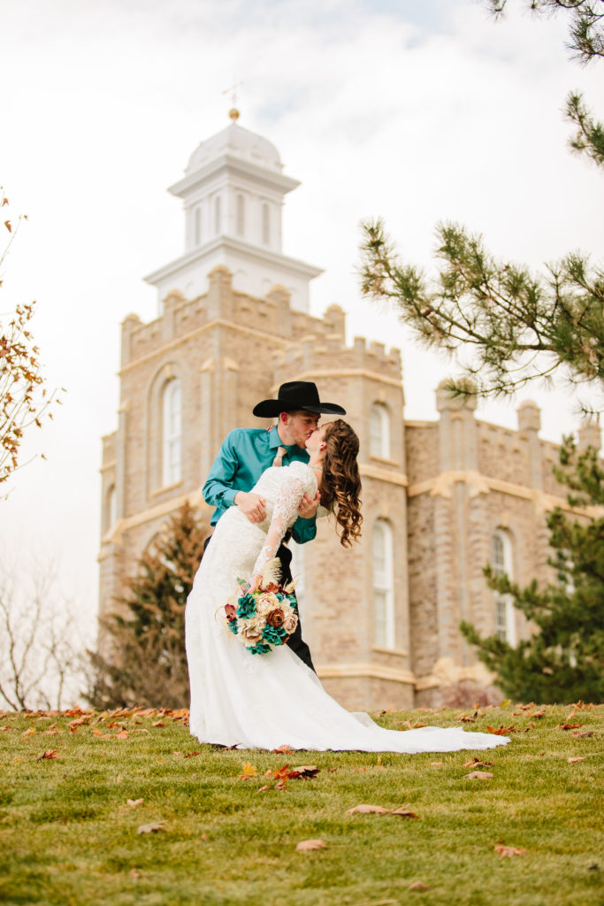 bride and groom kissing outside of the Logan temple in Utah with the groom in a black cowboy hat