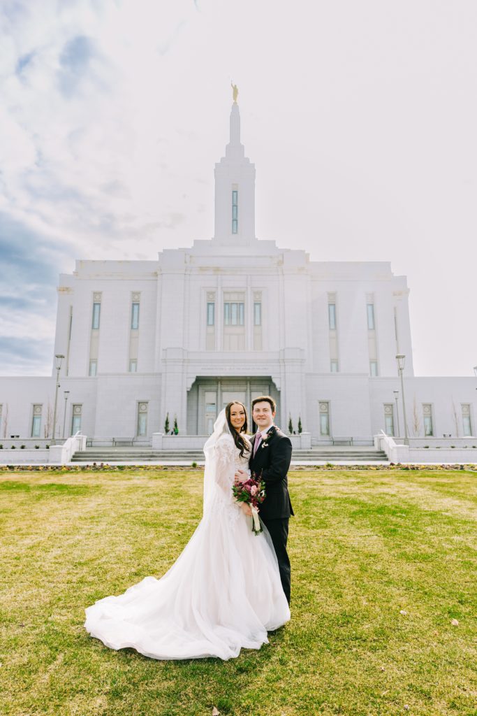 bride and groom standing on front temple lawn smiling at camera during bright pocatello temple bridals in pocatello idaho lds temple