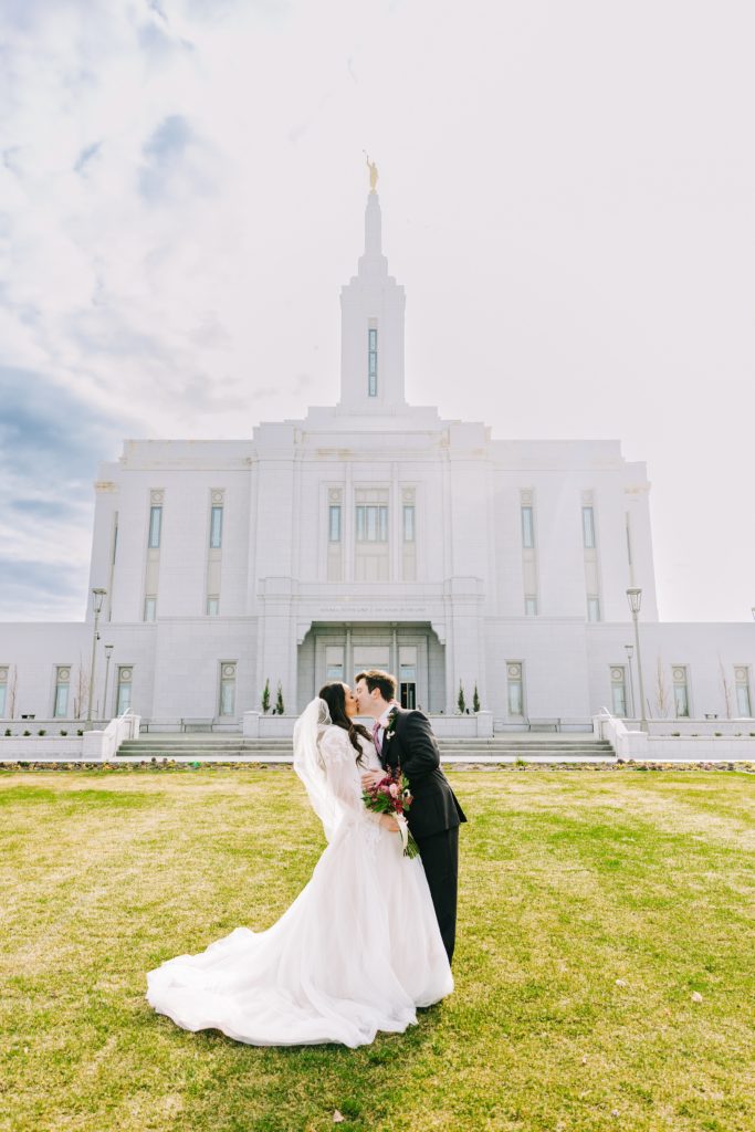 Bride and groom on green lawn of pocatello temple kissing during bright pocatello temple