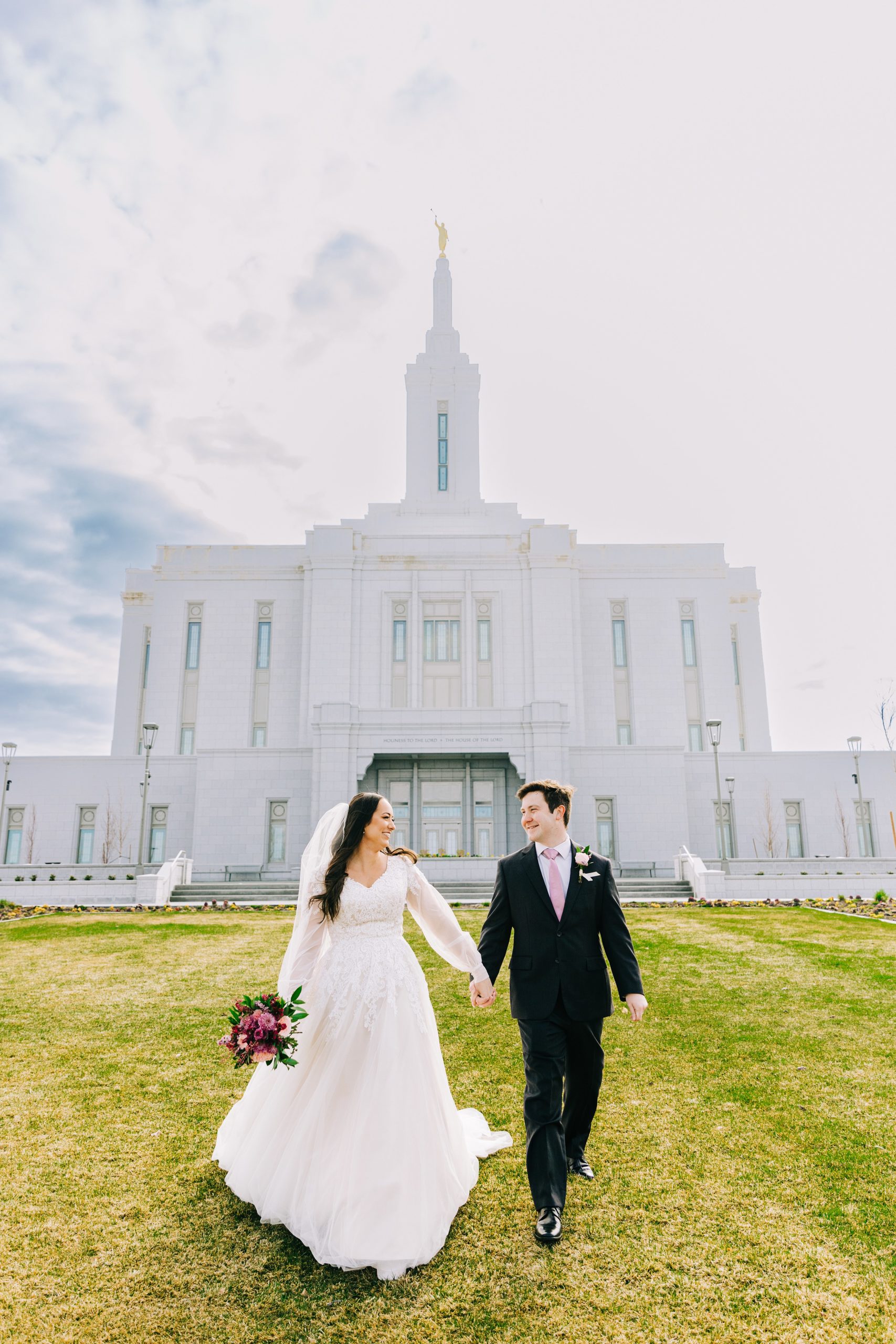 bride and groom walking down green lawn with pocatello temple behind them