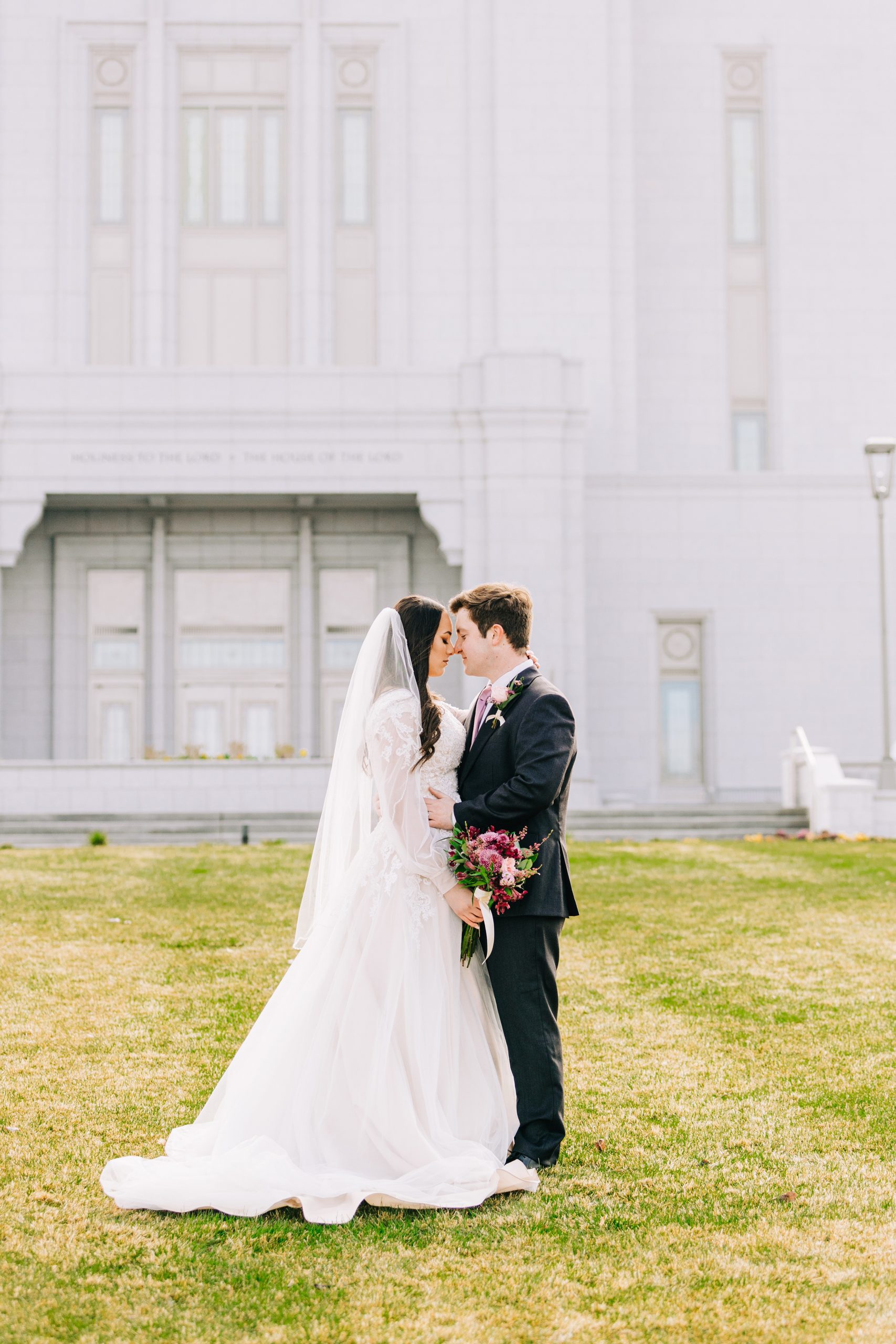 bride and groom place their heads together and embrace in love on lawn of pocatello lds temple
