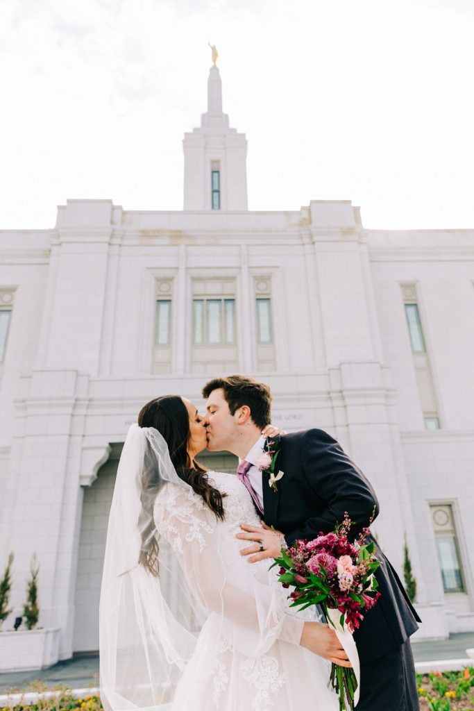 bride with purple and pink flowers from staker floral kiss groom at pocatello temple bright pocatello temple bridals