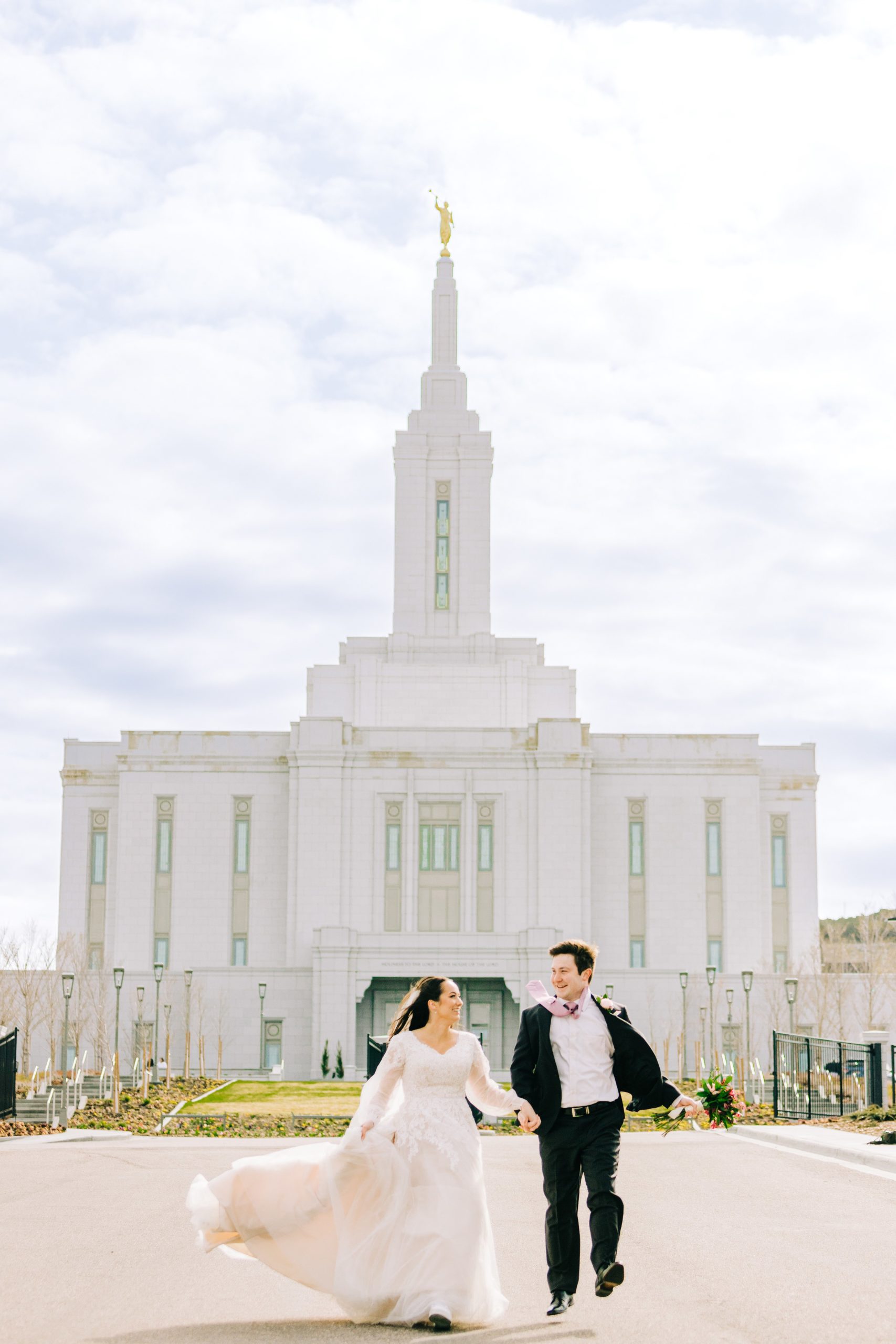 bride swishing her dress as she runs with husband from wedding day at pocatello temple
