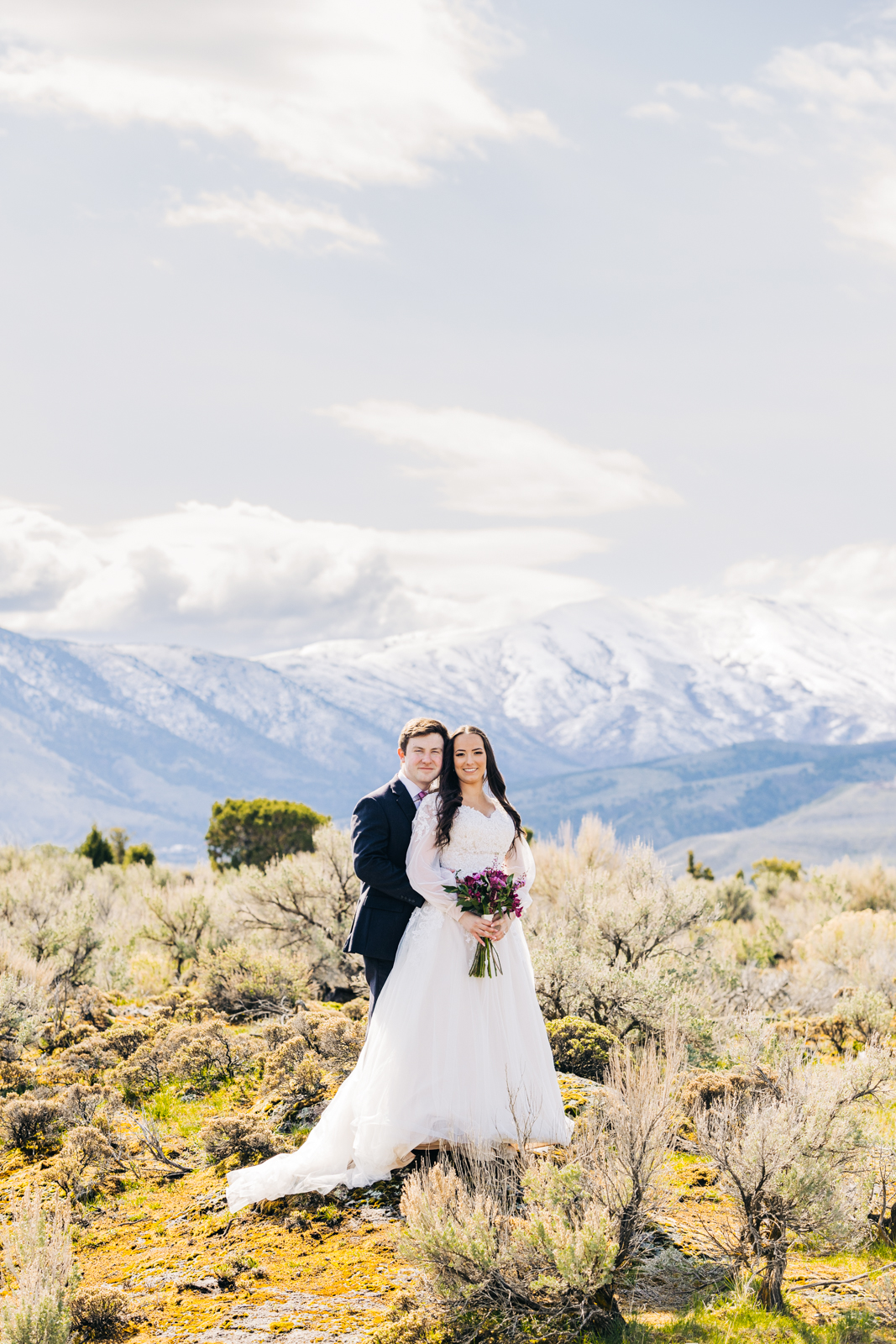 Jackson Hole wedding photographer captures bride and groom look at camera with the mountains behind them in pocatello wedding