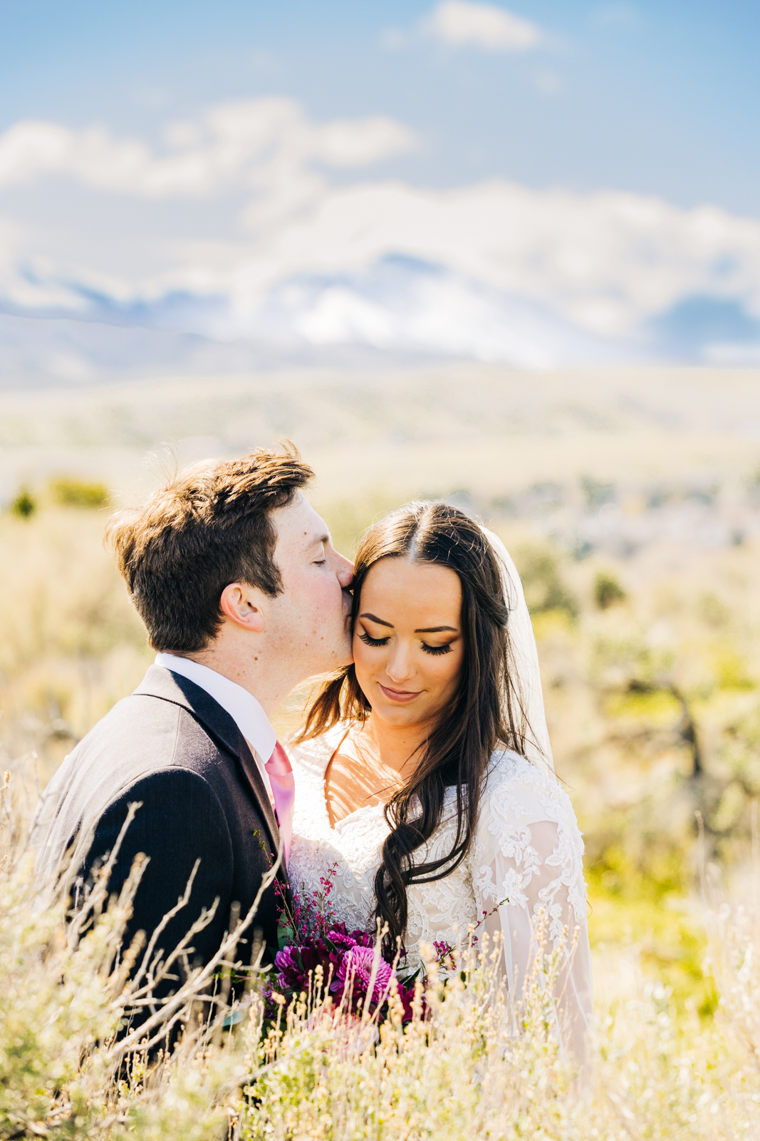 Jackson Hole wedding photographer captures groom kissing brides head as she looks down her shoulder in sagebrush