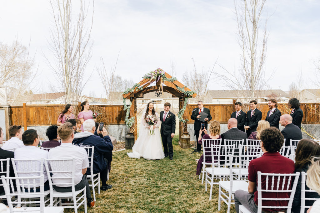 outdoor wedding ceremony in Idaho with bride and groom under an arch and walking towards the camera down the aisle